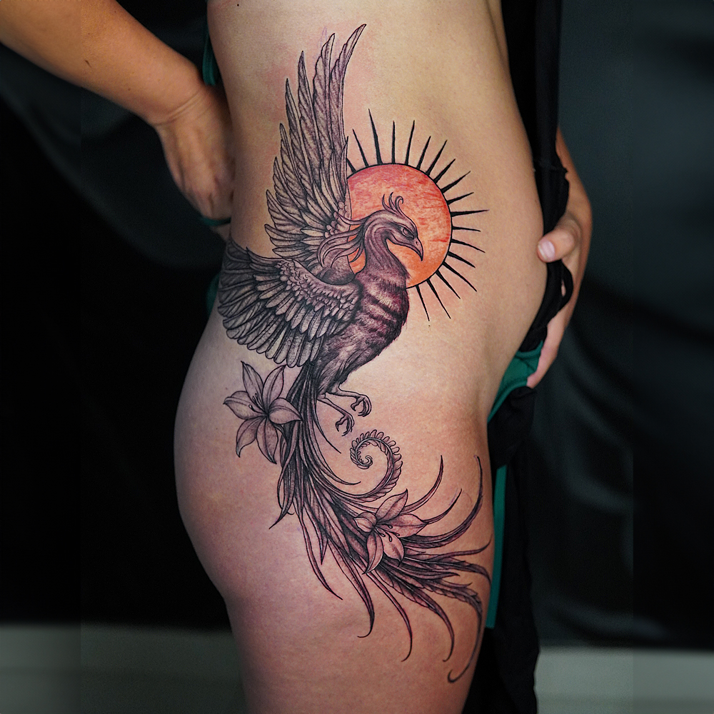 Phoenix Thigh Tattoo Design Large thigh tattoo of a phoenix with spread wings, red sun background, and floral elements in fine line style.