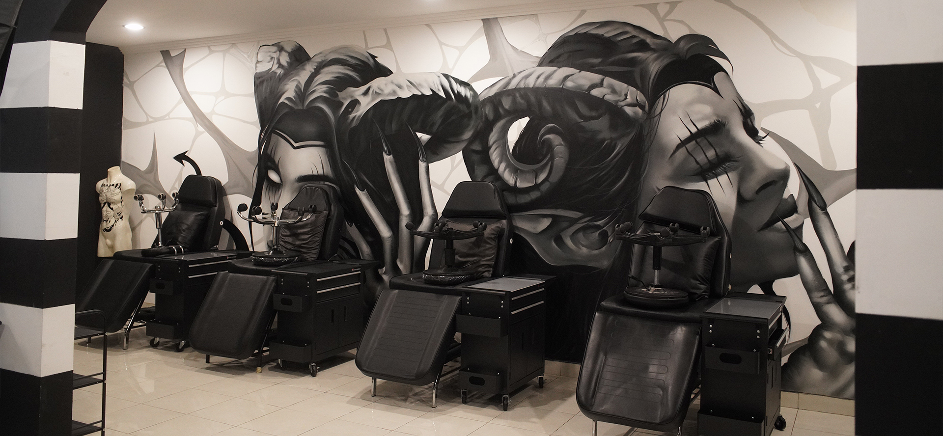 Inside Downunder Tattoo Bali: a row of black tattoo chairs and workstations in front of a large black and white mural of a woman's face